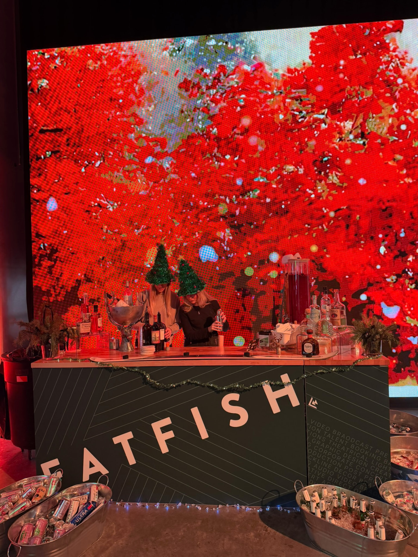 Hosts tending a holiday bar against a warm red light wall