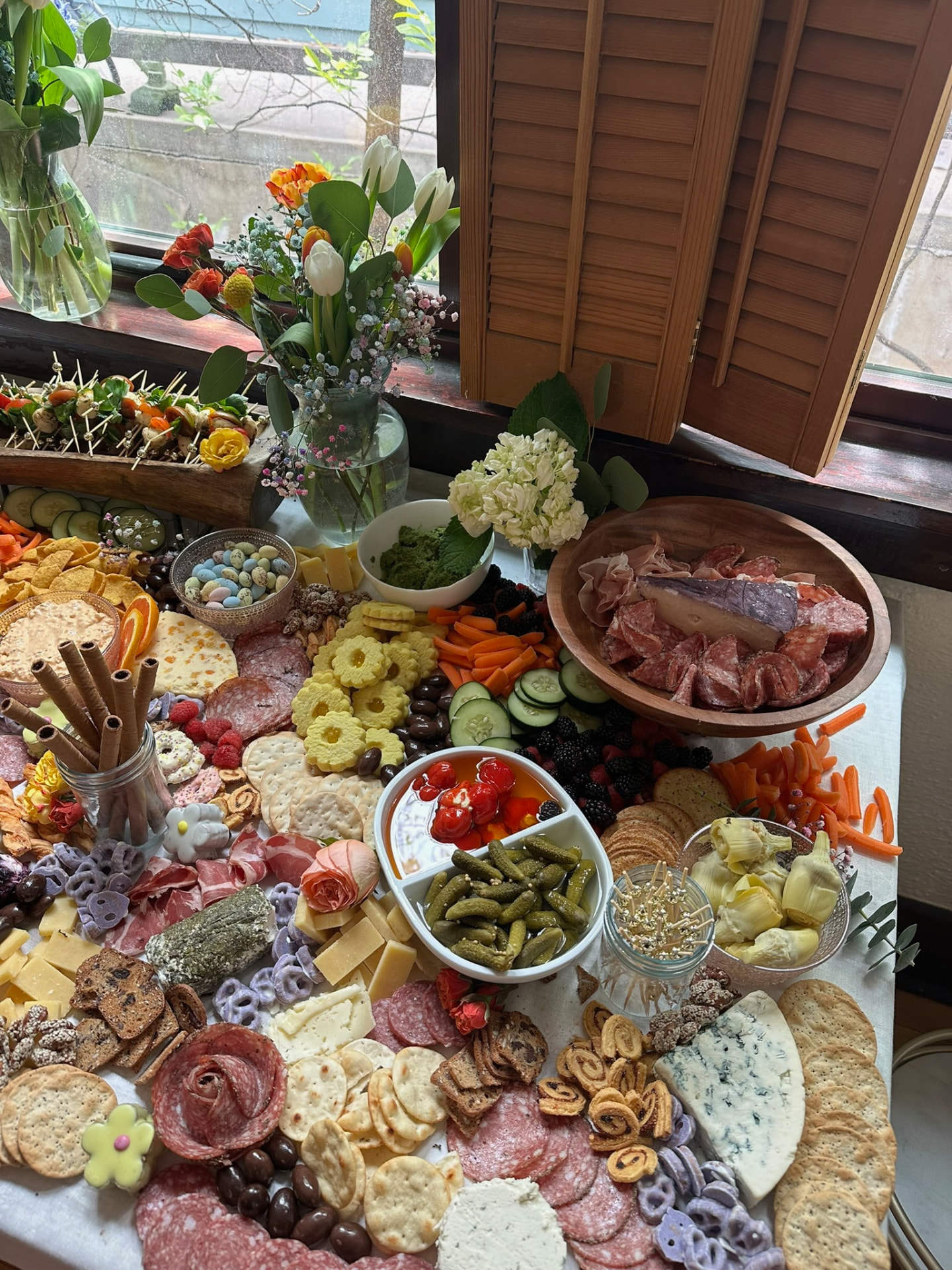 Spring grazing table with tulips, charcuterie, cookies and fresh fruit by a window