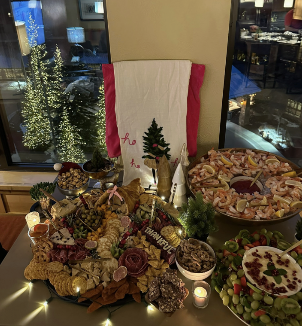 Holiday grazing spread with shrimp platter and lit trees beyond the window