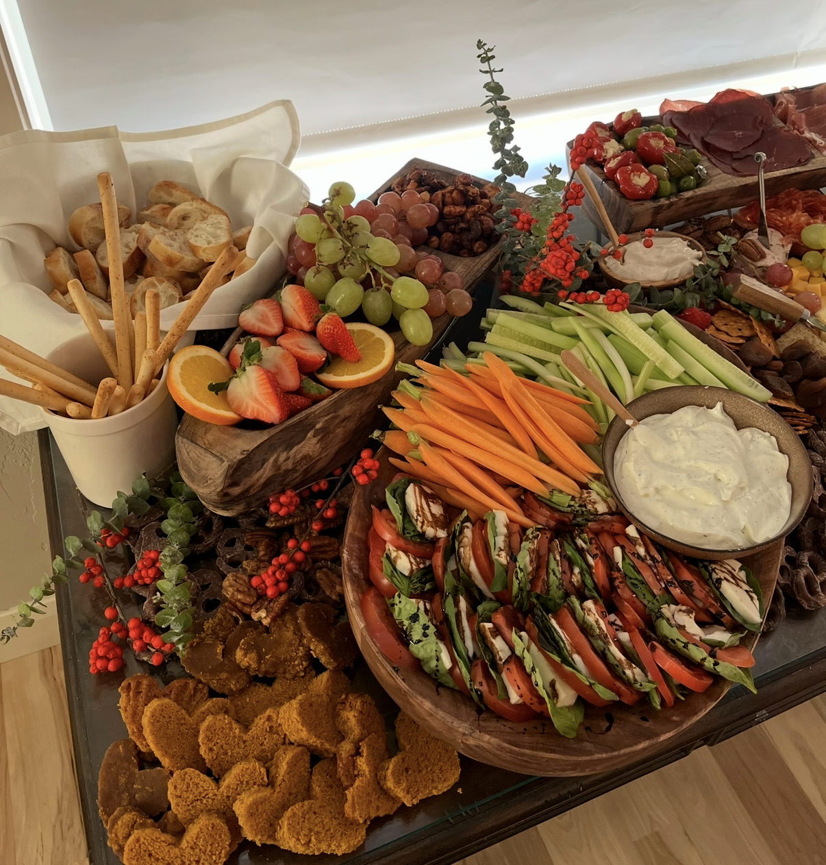 Layered spread with caprese, crudité, breads and grapes on wooden boards